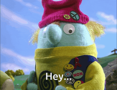 a stuffed animal wearing a pink hat and a yellow vest that says hey