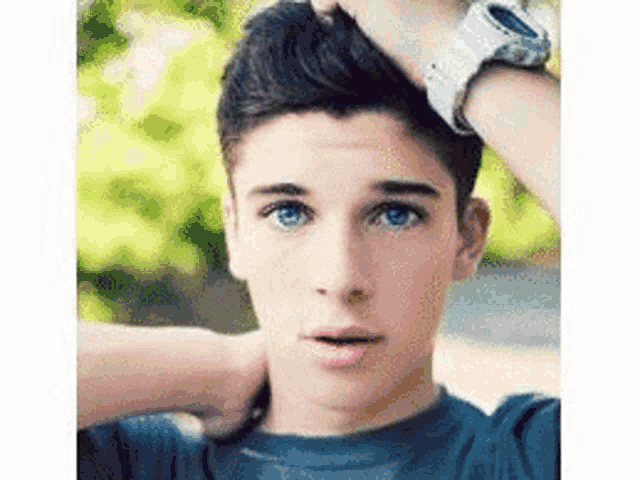 a young man with blue eyes and a watch on his wrist is holding his head .