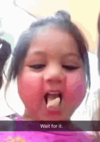 a little girl is eating a piece of food with the words wait for it written on the bottom