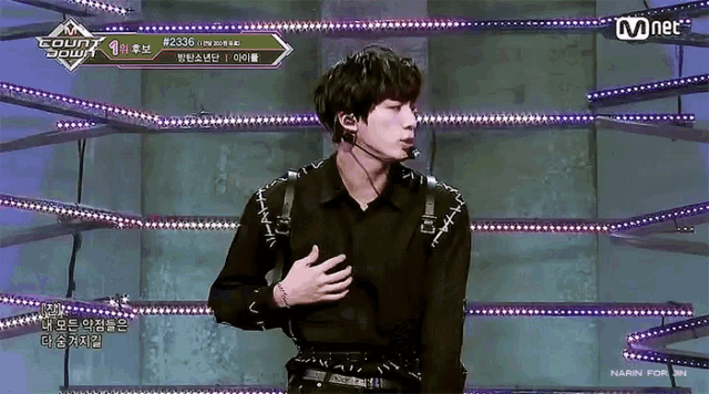 a man in a black shirt is standing on a stage with a microphone in his mouth and a sign that says mnet on it