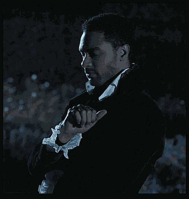 a man in a black suit with white cuffs is giving a thumbs up sign