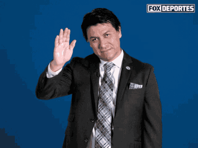a man in a suit and tie waves in front of a fox deportes logo