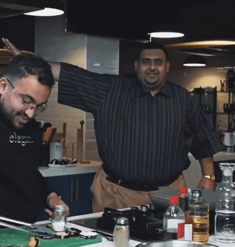 two men in a kitchen with one wearing a shirt that says elomar