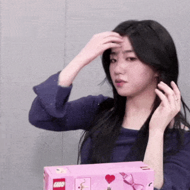 a girl is holding a pink lego box and touching her hair