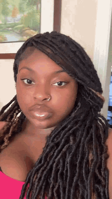 a woman with dreadlocks and a nose ring is wearing a pink top