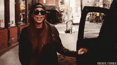 a woman wearing sunglasses and a hat is getting out of a car on a city street .