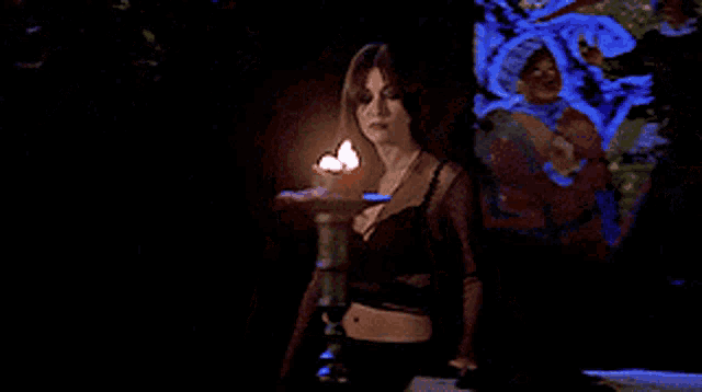 a woman in a black top is standing in front of a candle in a dark room .