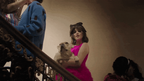a woman in a pink dress is holding a dog