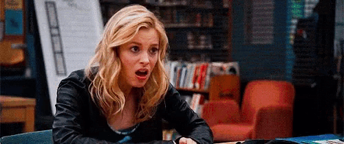 a woman in a leather jacket is sitting at a table in a library .