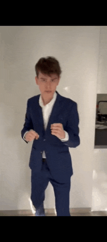 a young man in a suit is standing in front of a white wall .