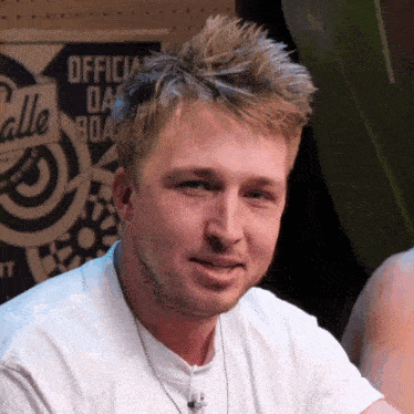a man wearing a white shirt and a necklace looks at the camera