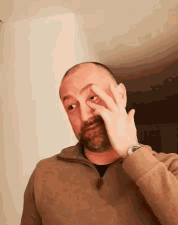 a bald man with a beard is covering his face with his hand