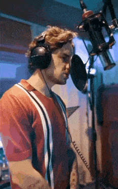 a man wearing headphones is singing into a microphone in a studio .
