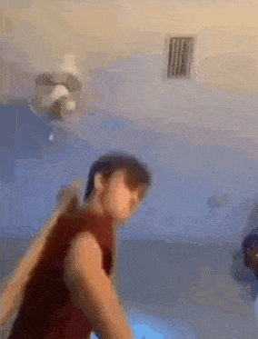 a blurry picture of a man standing in a room with a fan on the ceiling .