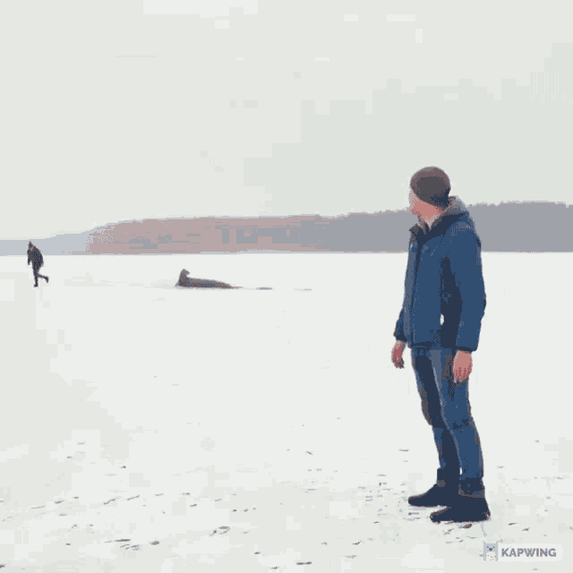 a man in a blue jacket is standing on a snowy beach with a caption in a foreign language