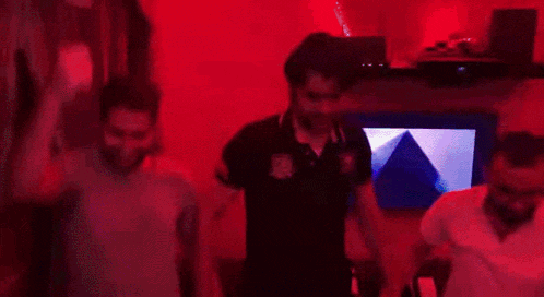 a group of men are dancing in a dark room with a green light behind them .