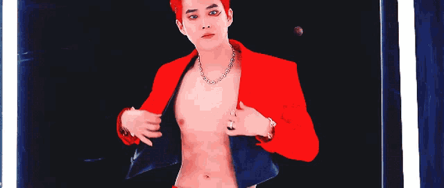a shirtless man wearing a red jacket and a chain necklace