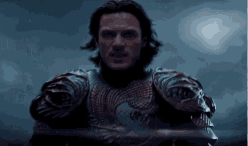 a man in armor is holding a sword in his hand in the dark .