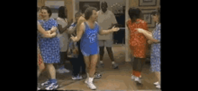 a group of people are dancing in a room while wearing dresses and shorts .