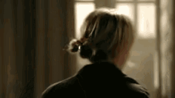 a woman with her hair in a bun is standing in front of a window in a room .