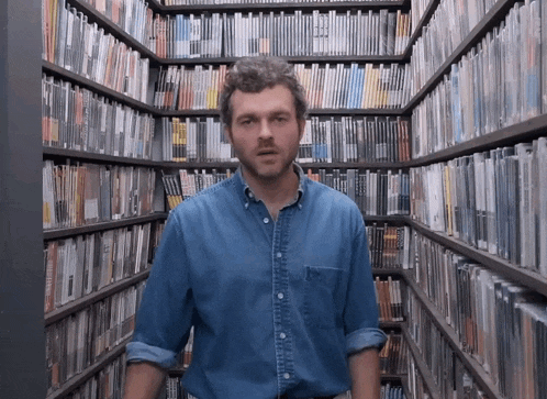 a man in a denim shirt stands in a library filled with books