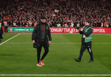a man walking on a soccer field in front of a liverpool sign