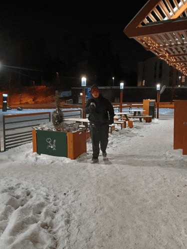 a man is walking in the snow near a green planter with a snoopy on it