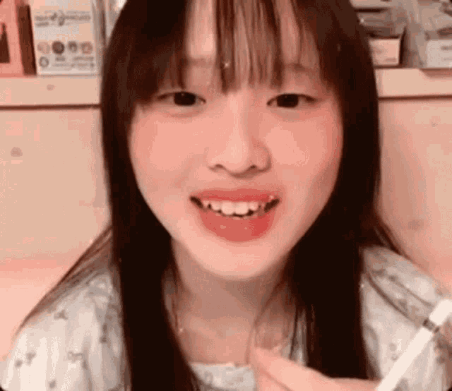 a young girl with long black hair and red cheeks is smiling and holding a cigarette .