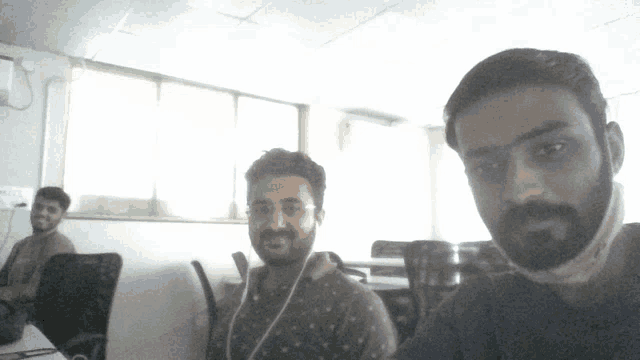 a man wearing a mask looks at the camera while another man sits behind him