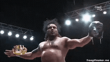 a shirtless wrestler is holding a mask in his hand in front of a claro sports sign