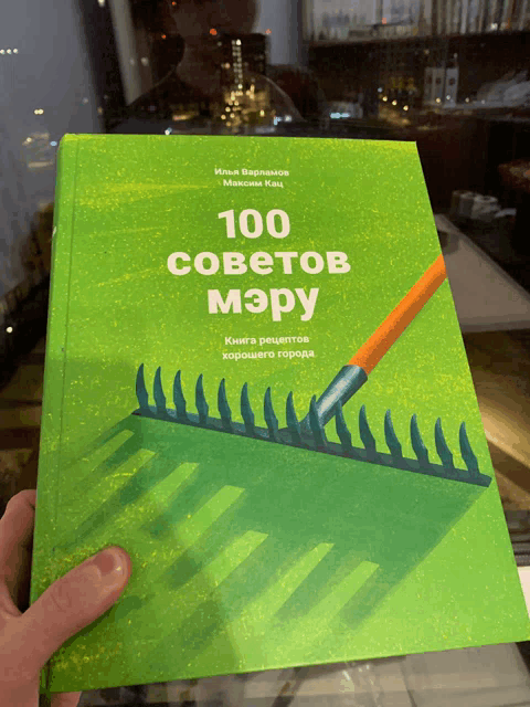 a green book titled 100 советов мэру is being held in someone 's hand