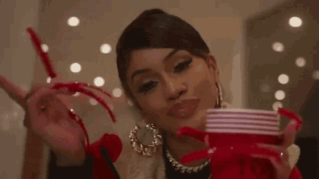 a woman with very long nails is holding a red cup and making a peace sign .