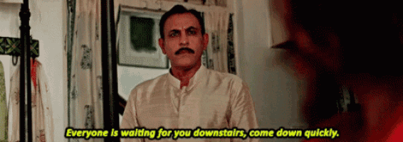 a man with a mustache is waiting for someone to come down the stairs in a room .