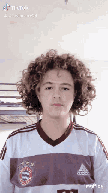 a young man with curly hair is wearing an adidas shirt