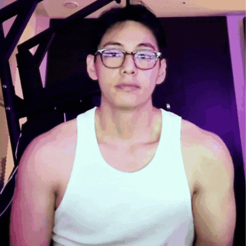 a man wearing glasses and a white tank top is standing in front of a purple wall