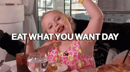 a little girl is sitting at a table eating spaghetti with the words `` eat what you want day '' above her .