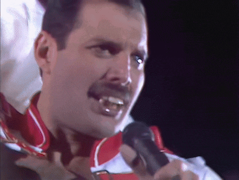 a man with a mustache is singing into a microphone in a dark room .