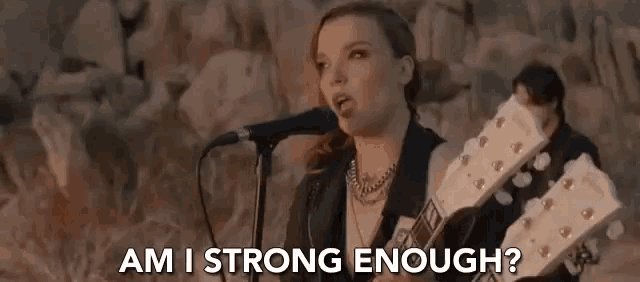a woman is singing into a microphone while holding a guitar in front of a man .
