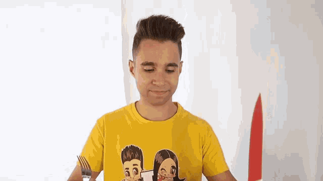 a man in a yellow t-shirt is holding a fork and knife .