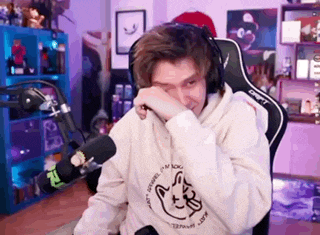 a man wearing headphones and a hoodie is sitting in a chair in front of a microphone .
