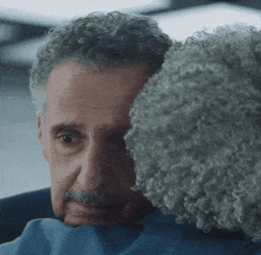 a man with curly hair is hugging another man in a blue shirt