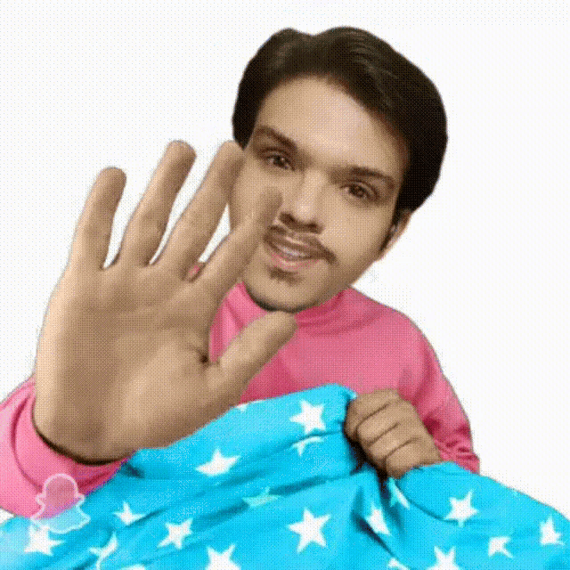 a man in a pink shirt is holding a blue blanket with stars on it and waving his hand .