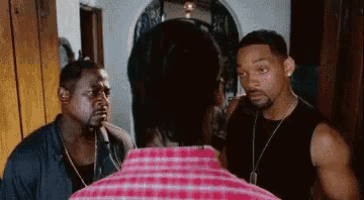 two men are standing next to each other in a room talking to each other .