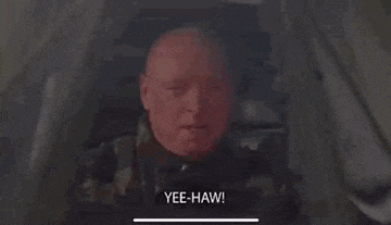 a bald man is sitting in a tent with his mouth open and saying yee-haw .