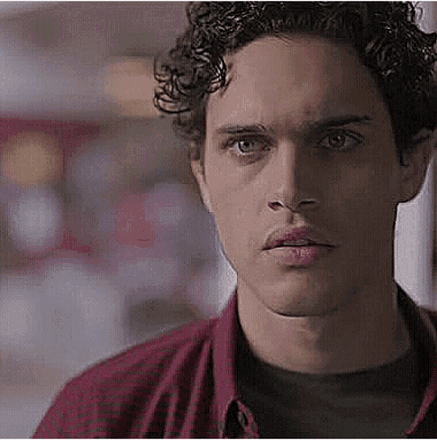 a close up of a young man 's face with curly hair wearing a red shirt .