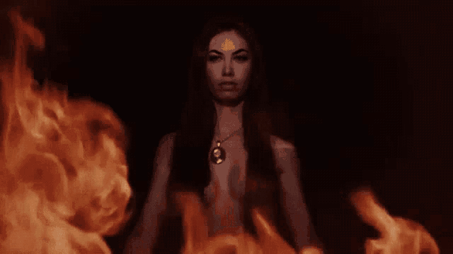 a woman is surrounded by flames in a dark room in a painting .