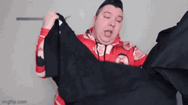 a man in a red hoodie is holding a black shirt