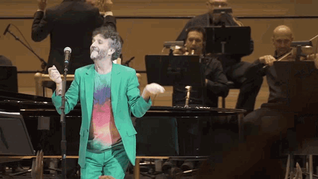 a man in a green suit is singing into a microphone in front of an orchestra