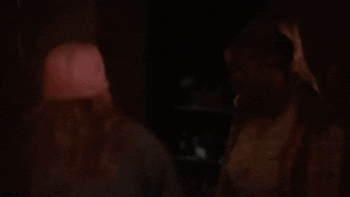 two women are standing next to each other in a dark room and talking to each other .
