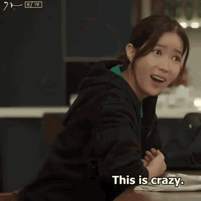 a woman is sitting at a table and making a funny face with the words `` just crazy '' next to her .